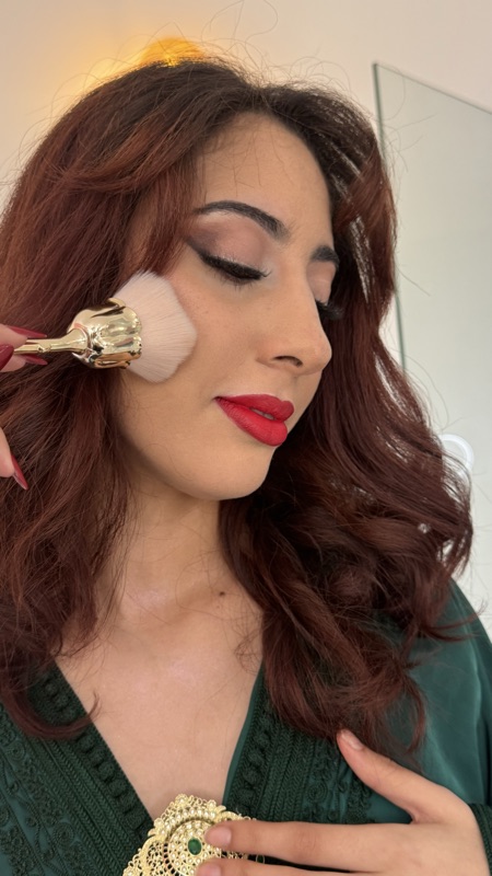 Makeup artist applying blush with a gold brush to a client with a red lip