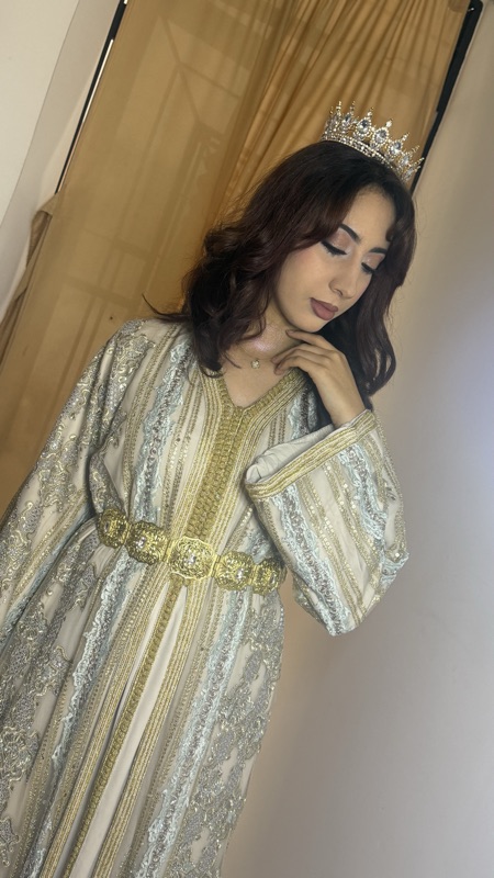 Bride in a silver and gold caftan with a jewelled belt, hand raised to her neck