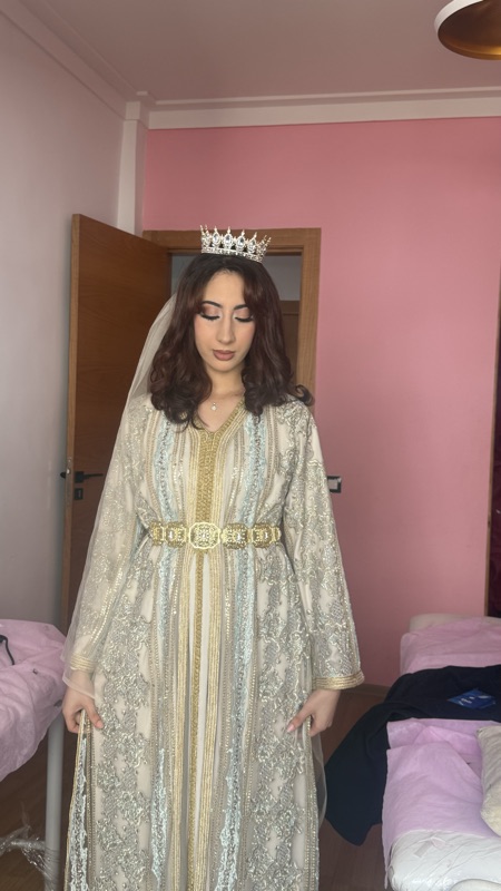 Full-length photograph of a Moroccan bride wearing a gold and silver takchita with a wide belt, veil and crown
